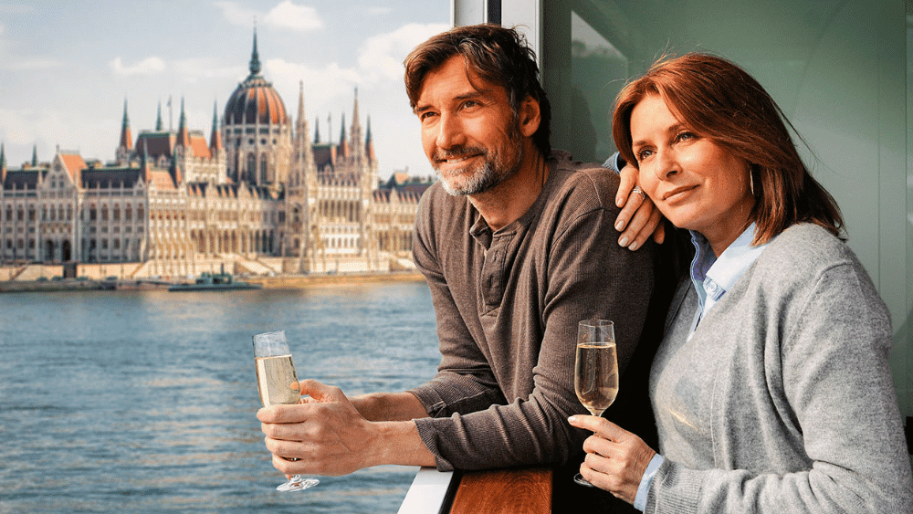 A couple enjoying a glass of wine on a boat, surrounded by picturesque views on a luxury river cruise in Europe.