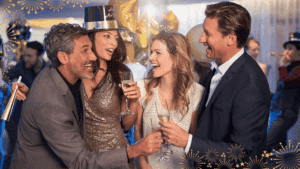 A festive group of friends toast with drinks at New Year's Eve while onboard on a cruise, surrounded by balloons.